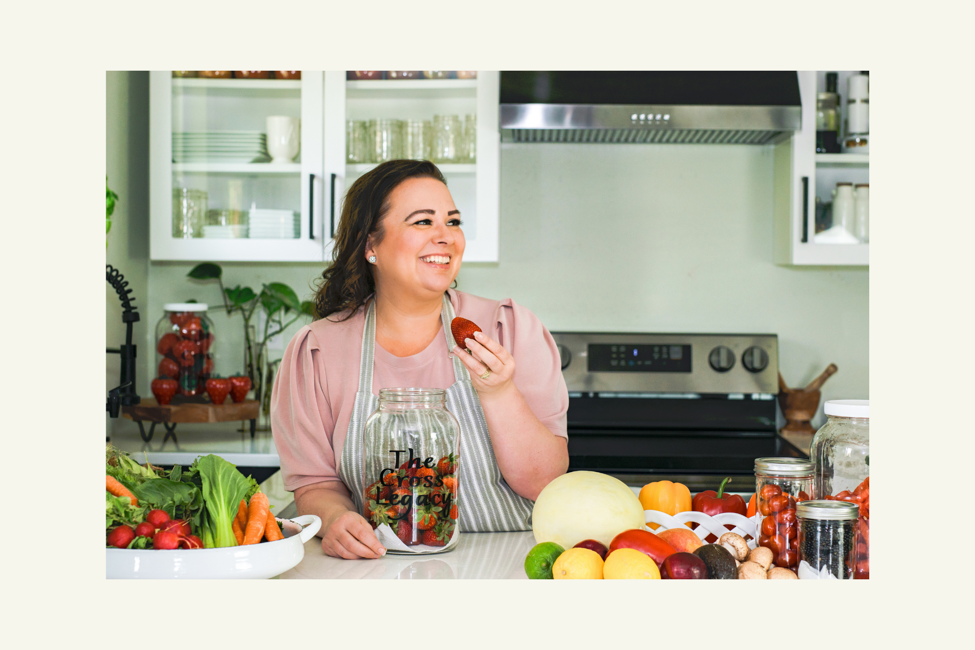 amy-cross-in-her-kitchen-holding-a-strawberry-with-a-counter-full-of-beautiful-fresh-produce