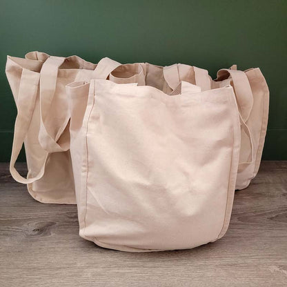 3 organic cotton canvas market bags sitting on the floor against a green wall