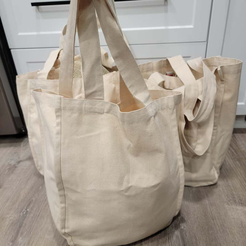 3 organic cotton canvas market bags sitting on the floor filled with produce in the kitchen