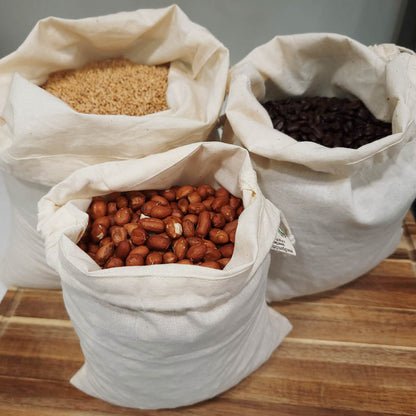 3 muslin bags filled with rice, coffee beans, and nuts sitting on a wooden cutting board
